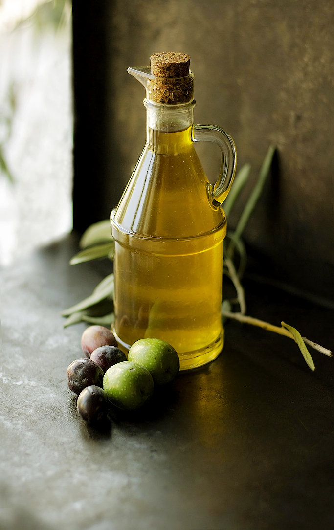 A bottle of olive oil on a counter with olives nearby.