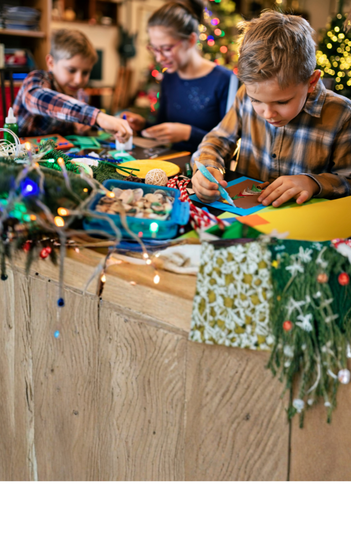 two children and a woman sitting at a table making holiday crafts