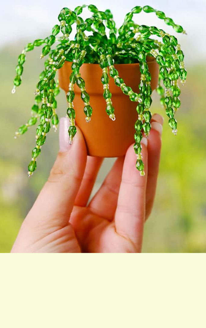 a hand is holding up a potted plant made from shiny beads and jewelry wire